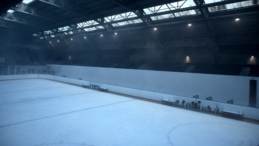 Wide interior of an empty ice hockey rink at dawn with freshly resurfaced ice, half-lit house lights and empty player benches along the boards
