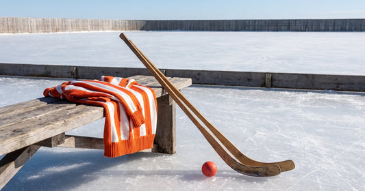 Curved wooden bandy hockey stick and small orange ball on outdoor ice beside an orange and white striped jersey