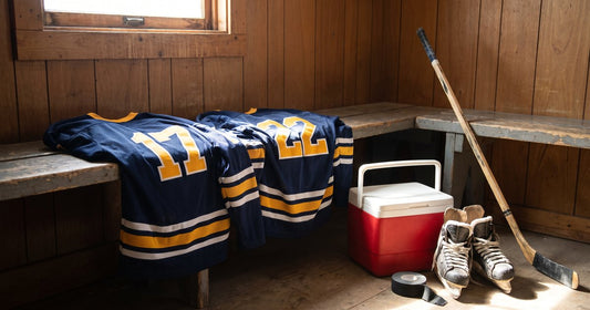 Navy and gold custom beer league hockey jerseys #17 and #22 on a locker room bench with a red cooler and skates