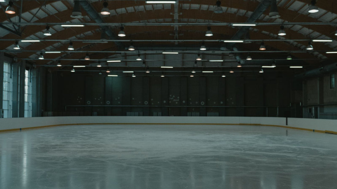An empty indoor ice rink lit by overhead arena lighting