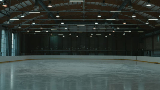 An empty indoor ice rink lit by overhead arena lighting