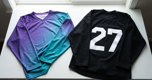 Purple to teal sublimated hockey jersey laid beside a black jersey with a white tackle twill number 27