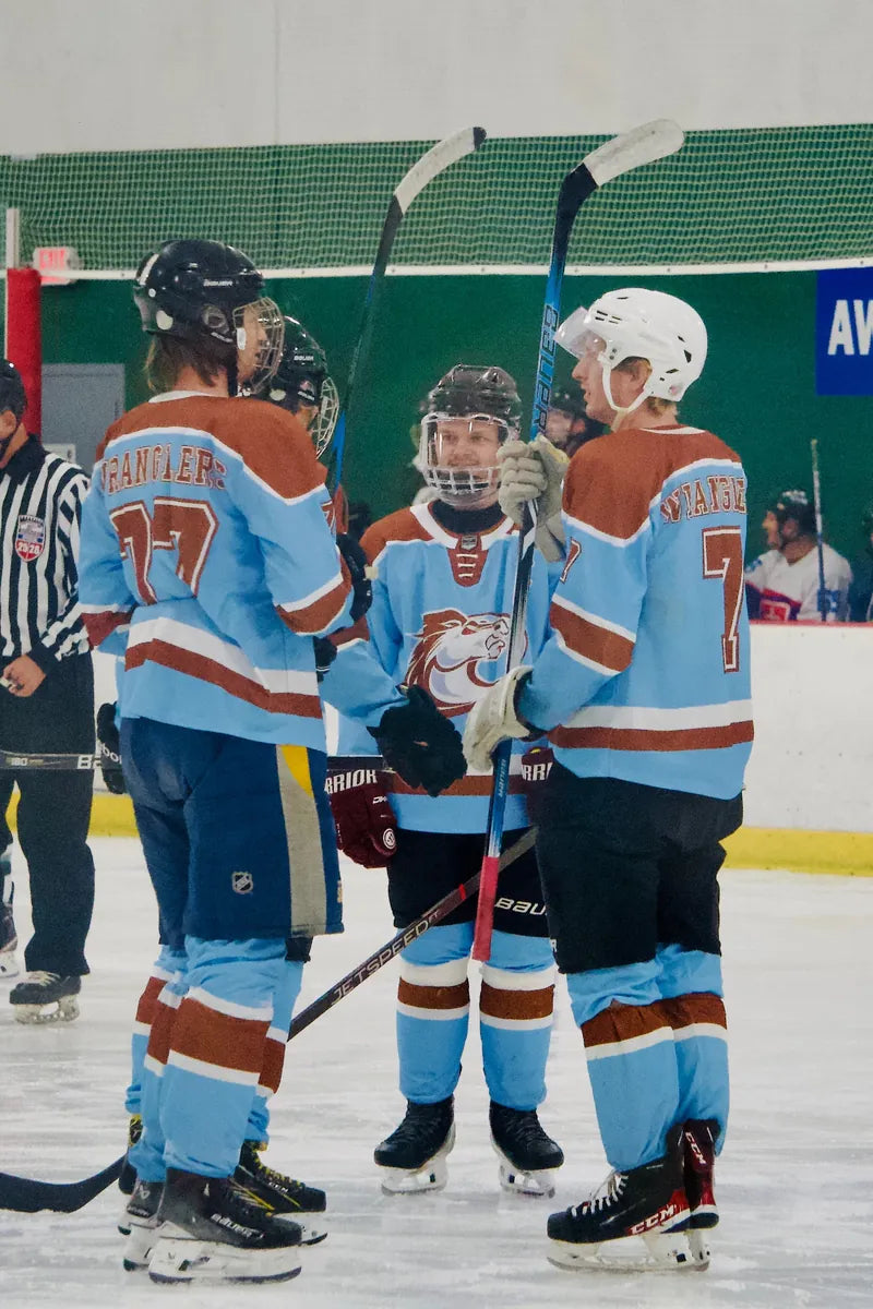 Three Austin Wranglers players in light blue and maroon custom jerseys at the bench